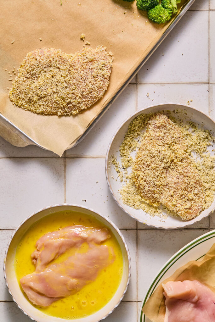 A chicken cutlet in a bowl of beaten eggs and a bowl of breadcrumbs.