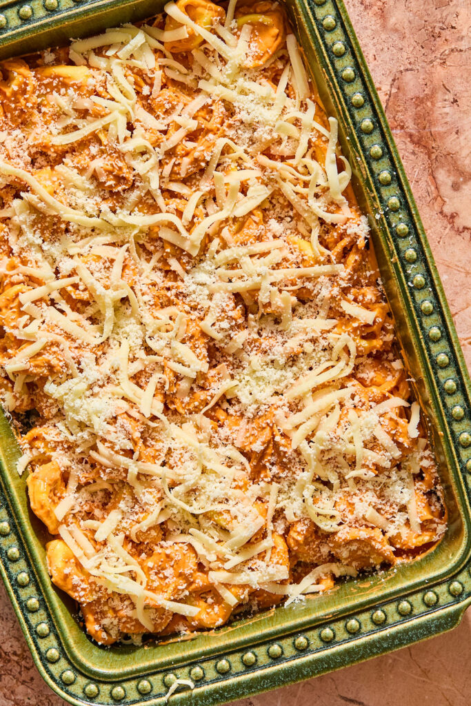 Chicken Parmesan Tortellini Bake in baking dish topped with shredded cheese before being baked.