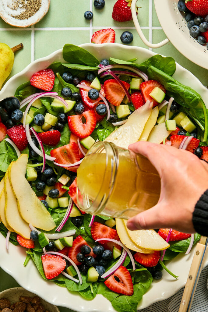Dressing being poured over the Rainbow Spinach Summer Salad in a bowl.