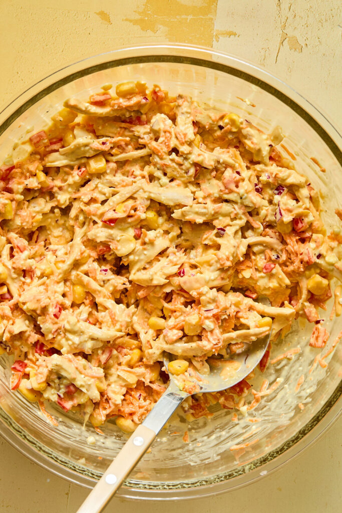 Chicken and veggies and honey mustard mixture combind in a bowl with a spoon.